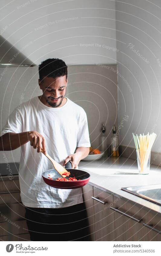 Inhalt ethnischer Mann brät Tomaten in der Pfanne in der Küche Koch vorbereiten braten mischen Lebensmittel Bestandteil Spachtel jung rühren positiv Prozess