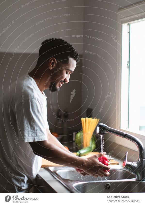 Ethnischer Mann wäscht Paprika bei der Zubereitung von Speisen Waschen Küche Waschbecken Koch Wasser vorbereiten Vegetarier frisch gesunde Ernährung lässig
