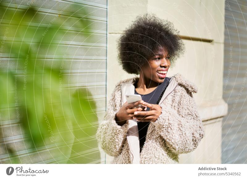 Aufgeregte ethnische Frau mit Smartphone in der Stadt Texten Glück heiter urban Lächeln Funktelefon Gerät Apparatur positiv Freude Afroamerikaner jung Lifestyle