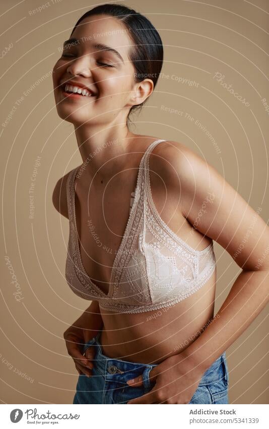 Fröhliche Frau in Unterwäsche lächelt mit geschlossenen Augen Lächeln Glück Augen geschlossen positiv BH Porträt heiter Stil Jeanshose jung Freude Model
