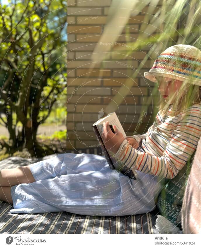 Mädchen sitzt draußen auf einer Decke und liest in einem Buch Kind lesen lernen Kindheit Literatur Konzentration Gesicht Interesse Sonnenlicht Gräser Wand