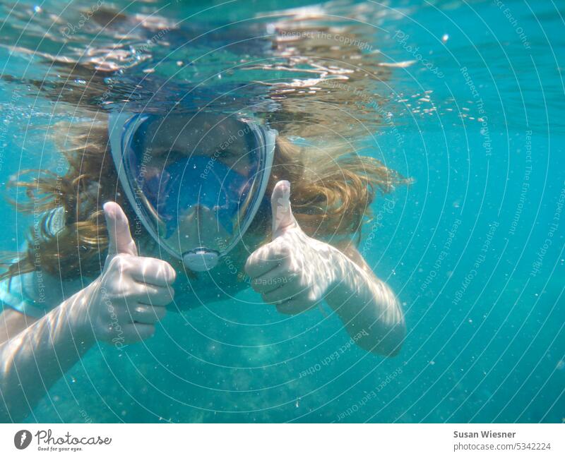Mädchen mit langen Haaren und Schnorchelmaske im türkisfarbenen Wasser blickt in die Kamera und gibt mit beiden Daumen das Zeichen für ok. Schnorcheln Meer