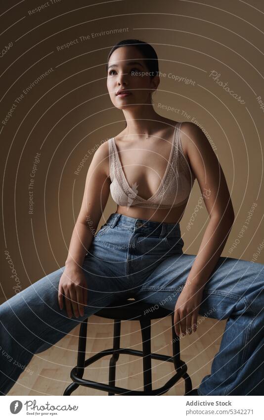Anmutige Frau sitzt auf einem Stuhl in einem hellen Studio Stil Dessous Porträt Model nachdenklich sinnlich Hocker Jeanshose Unterwäsche Figur Atelier