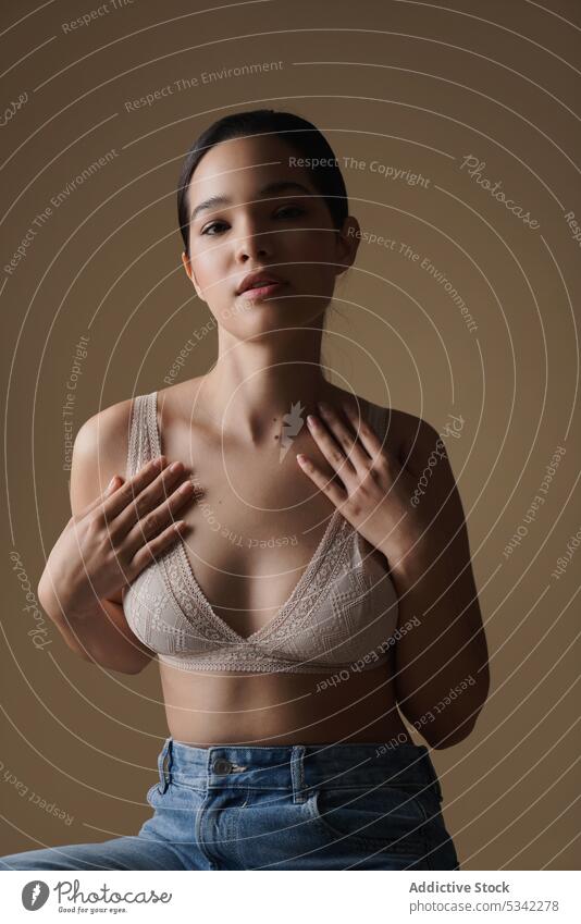 Ruhige Frau in Unterwäsche, die ihre Brust berührt und in die Kamera schaut Stil Model verträumt Porträt BH Brust berühren Atelier Schönheit Jeanshose schlank