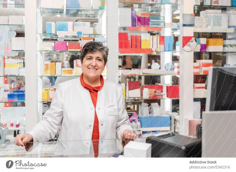 Fröhliche Frau in medizinischer Uniform schaut bei der Arbeit in die Kamera Drogerie Apotheker Tablette Medizin Lächeln Pharma Leckerbissen Medikament Vitrine