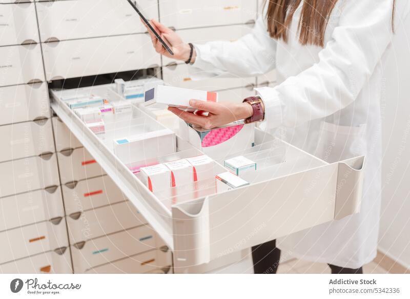 Crop Apotheker mit Tablette während stehend durch geschlitzte Regale mit Medikamenten in der modernen Apotheke Wissenschaftler Labor Frau Drogerie Laden