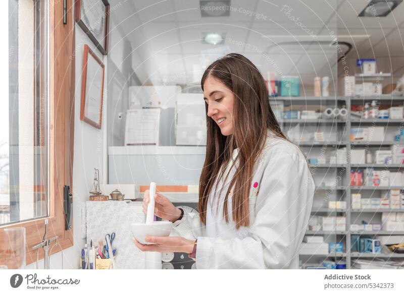 Glückliche Frau, die ein medizinisches Präparat bei der Arbeit in einer Drogerie zerkleinert vorbereiten Apotheker Minenwerfer Stössel Medizin Lächeln positiv