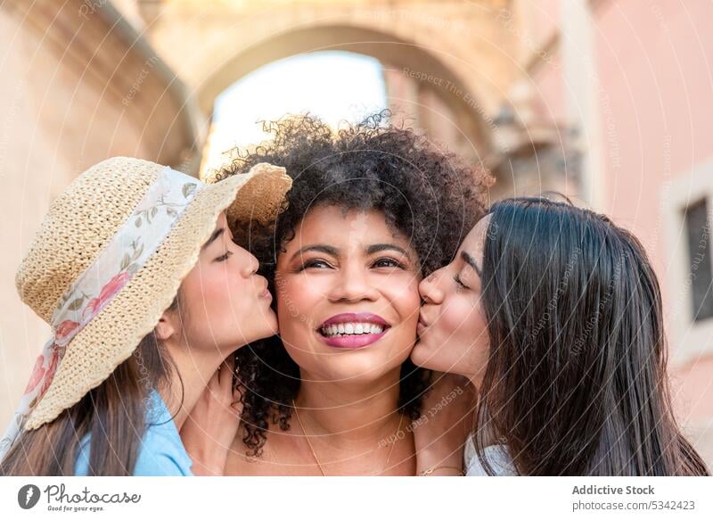 Glückliche verschiedene Freundinnen küssen schwarze Frau auf der Straße Frauen Großstadt Kuss Lächeln heiter positiv Partnerschaft Liebe rassenübergreifend