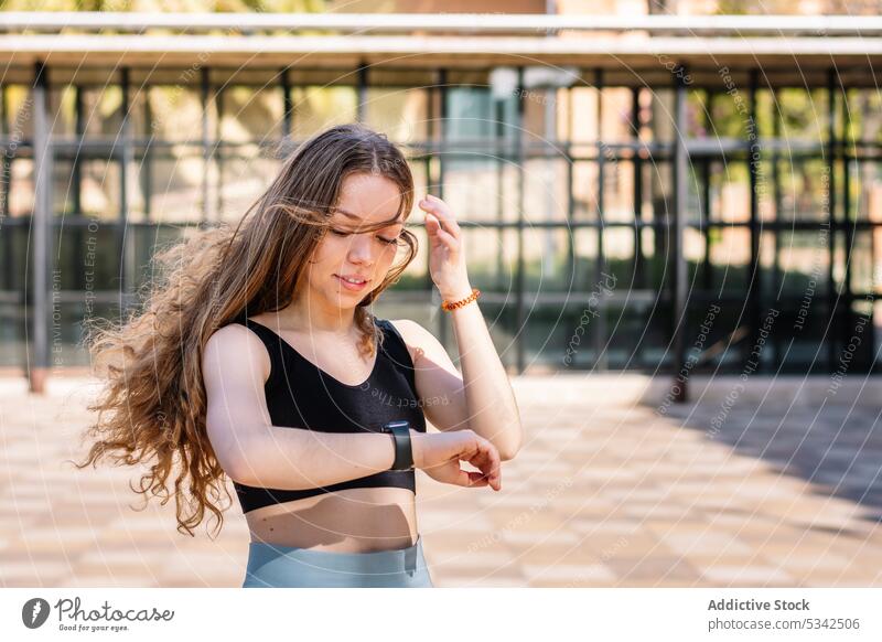 Junge Frau schaut auf ihre Armbanduhr prüfen positiv Zeit intelligente Uhr Training Straße Lächeln Fitness jung allein Übung Sportkleidung passen lange Haare