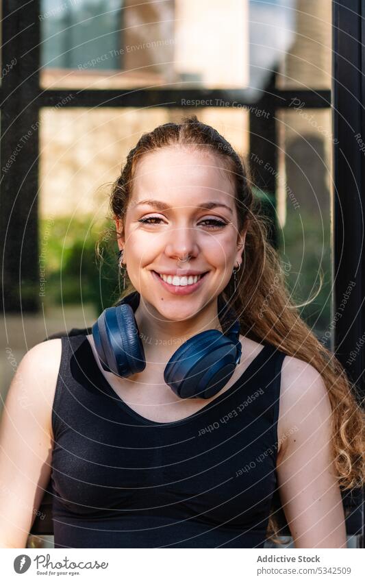 Lächelnde Frau mit Kopfhörern starrt in die Kamera Glück zuhören heiter Musik positiv Headset Porträt passen froh jung Drahtlos Optimist Zahnfarbenes Lächeln