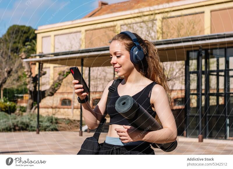 Lächelnde Frau mit Kopfhörern und Smartphone benutzend zuhören Musik Straße Spaziergang Unterlage Browsen Aktivität führen Gerät jung Surfen online