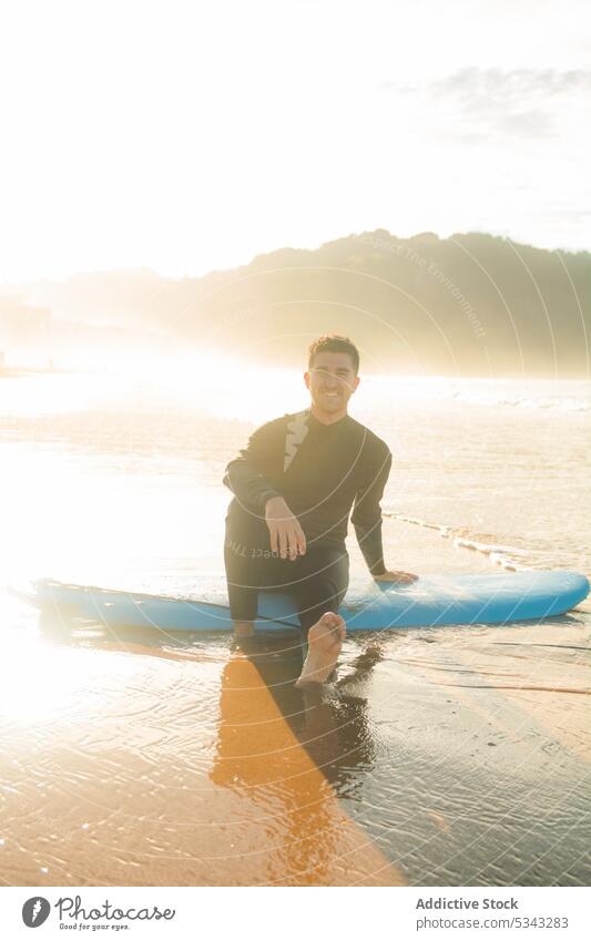 Mann sitzt auf Surfbrett am Strand Surfer MEER Sonnenuntergang winken Sport Meer Wasser Sommer Hobby männlich Aktivität jung Abend Küste Ufer