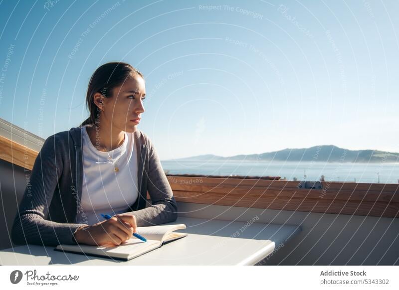 Verträumte Frau macht sich auf dem Balkon Notizen in einem Notizbuch zur Kenntnis nehmen Notizblock Notebook schreiben Schüler Denken Terrasse lernen
