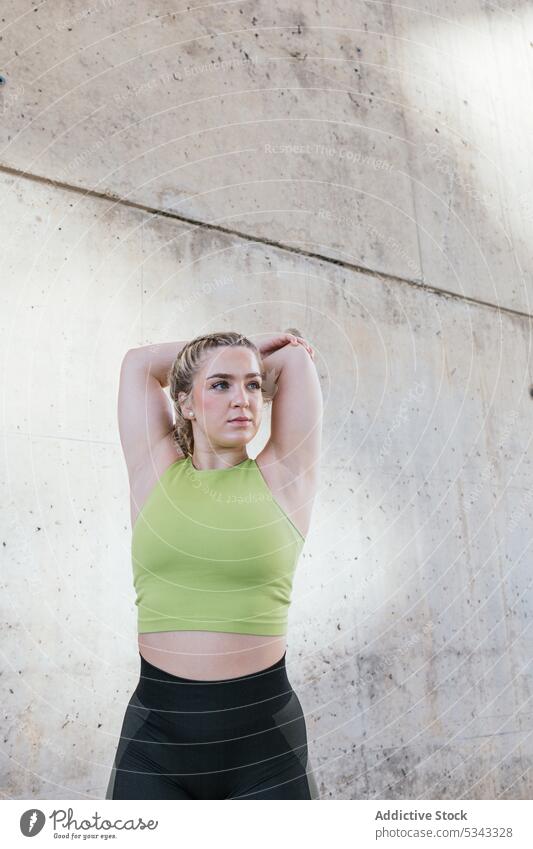 Junge Sportlerin streckt die Arme in der Nähe einer Betonwand Dehnung Training Übung Aufwärmen Fitness Wellness Gesundheit Frau Sportbekleidung jung Athlet