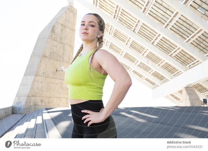 Sportlerin steht unter Sonnenkollektoren in der Stadt Frau Athlet passen Sportbekleidung selbstbewusst Konstruktion Fitness Training Hand auf der Taille Treppe