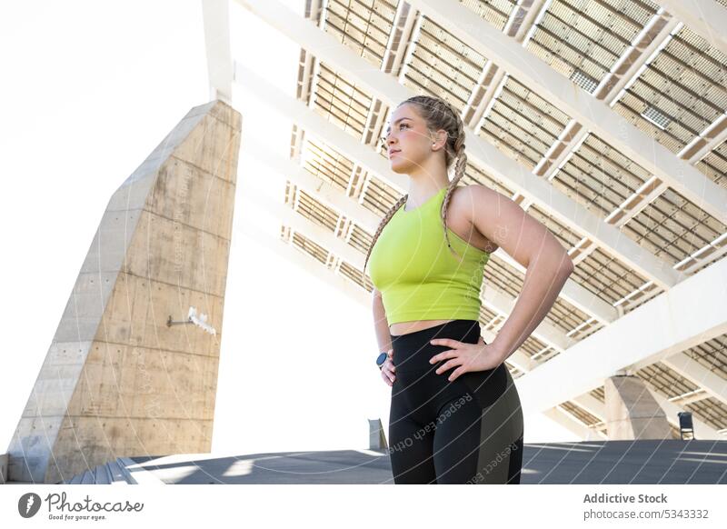 Sportlerin steht unter Sonnenkollektoren in der Stadt Frau Athlet passen Sportbekleidung selbstbewusst Konstruktion Fitness Training Hand auf der Taille Treppe