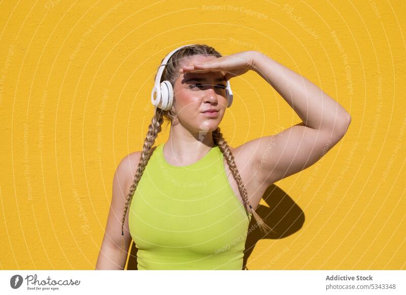 Junge Frau mit Kopfhörern in der Nähe eines gelben Hintergrunds stehend zuhören Musik Sonnenlicht Audio benutzend Fokus Drahtlos Sommer Melodie Gesang hell