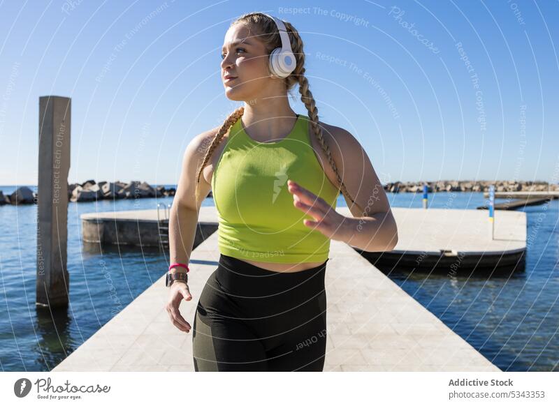 Fitte Sportlerin mit Kopfhörern beim Joggen auf der Seebrücke Frau Athlet Training laufen Pier Fitness Übung Gesundheit Wasser Wellness joggen Sportbekleidung