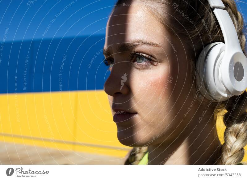 Junge Frau, die mit Kopfhörern Musik hört zuhören Porträt Geflecht selbstbewusst Schatten Farbe Wand Windstille jung hell lebhaft emotionslos Stil farbenfroh