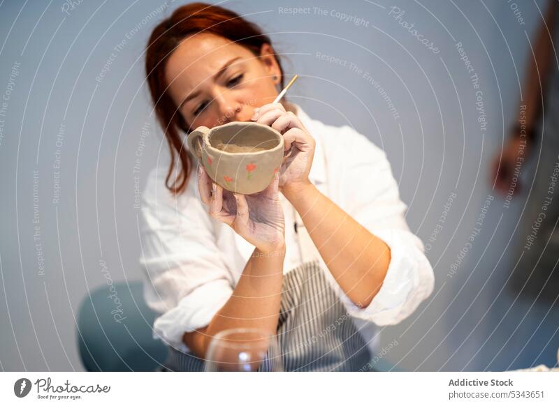 Konzentrierte Frau beim Bemalen einer Tontasse in einem Workshop Farbe Töpferwaren Werkstatt Tasse Meisterklasse Bürste Künstler kreieren handgefertigt Keramik