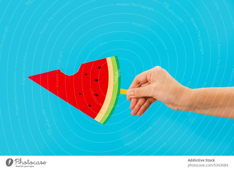 Crop anonyme Person zeigt Scheibe der künstlichen Wassermelone mit einem Biss aus Stieleis manifestieren Frucht Sommer lecker süß kreativ Hand Kunst Papier hell