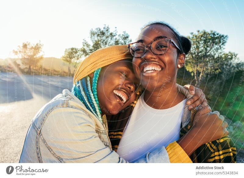 Fröhliche schwarze Frauen umarmen sich auf der Straße auf dem Lande Freund Umarmen Lachen heiter Freundschaft Natur Umarmung Freizeit Wochenende Afroamerikaner