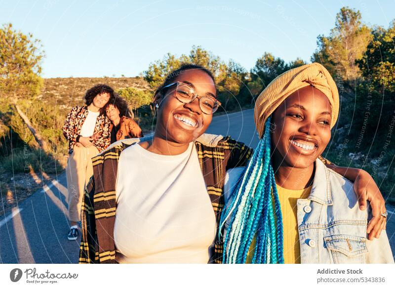 Glückliche schwarze Freunde, die bei Tageslicht am Straßenrand spazieren gehen Frauen Freundschaft Zeit verbringen heiter positiv Inhalt froh Bonden Outfit