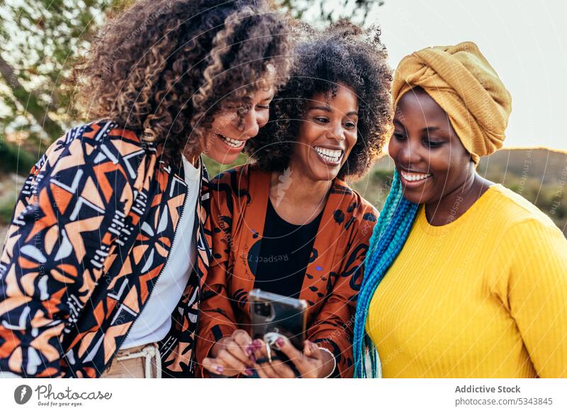 Fröhliche, unterschiedliche Freunde, die gemeinsam ein Smartphone benutzen benutzend Frauen heiter Zusammensein Browsen vielfältig rassenübergreifend