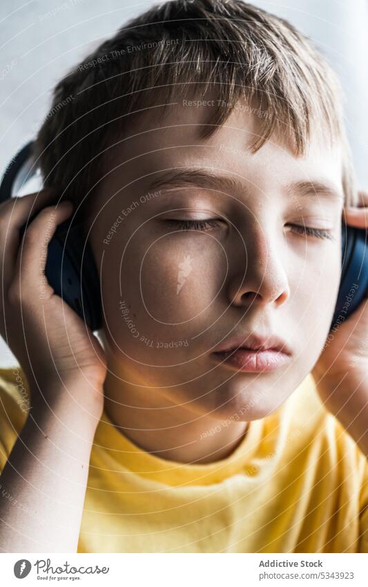 Porträt eines ernsten Kindes mit geschlossenen Augen, das Musik hört schön Junge Ohr Gesicht Kopfhörer menschlich zuhören über-Ohr Person T-Shirt Teenager