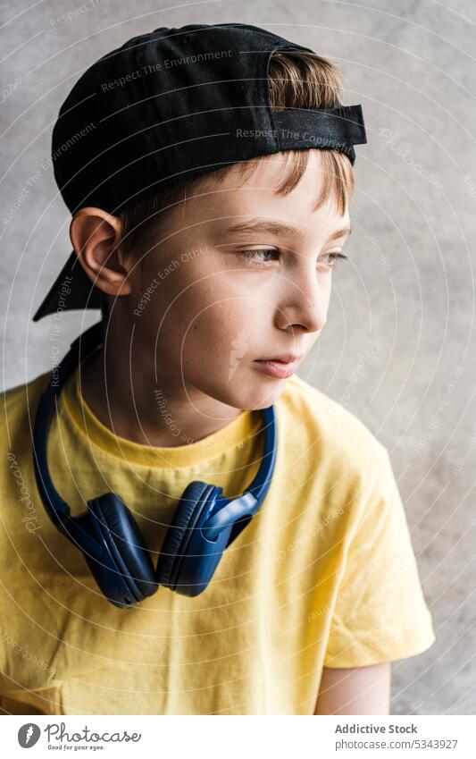 Seitenansicht eines nachdenklichen Jungen in gelbem T-Shirt und schwarzer Mütze mit Kopfhörern im Nacken, der vor einem unscharfen Hintergrund wegschaut schön