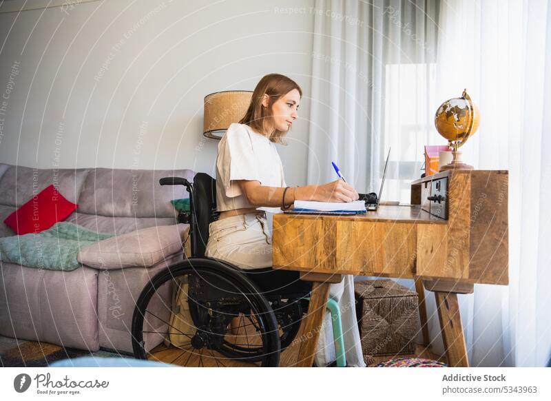 Junge Frau sitzt im Rollstuhl und macht sich Notizen am Laptop Notebook zur Kenntnis nehmen schreiben freiberuflich Sofa Wohnzimmer heimwärts benutzend