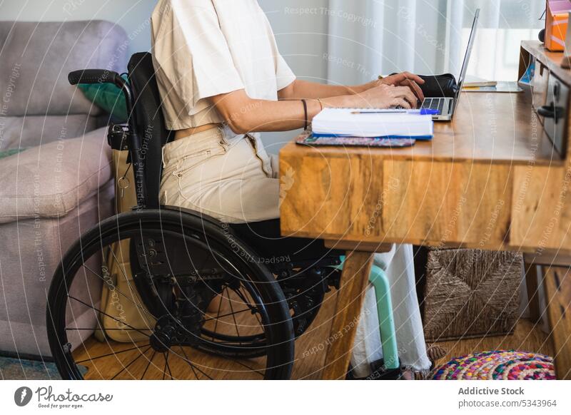 Abgeschnittener Körper einer jungen Frau, die auf einem Rollstuhl sitzt und sich Notizen auf einem Laptop macht Notebook zur Kenntnis nehmen schreiben