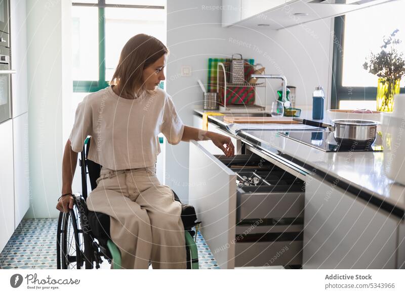 Junge Frau im Rollstuhl bei der Hausarbeit in einer modernen Küche heimwärts heimisch Arbeit Haushalt Appartement beschäftigt lässig Lifestyle deaktivieren jung