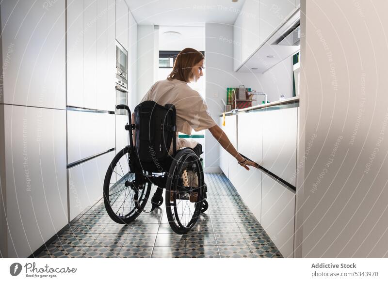 Junge behinderte Frau im Rollstuhl neben einem geöffneten Schrank in der Küche deaktivieren Kühlschrank Handicap zu Hause Appartement heimwärts lässig hungrig
