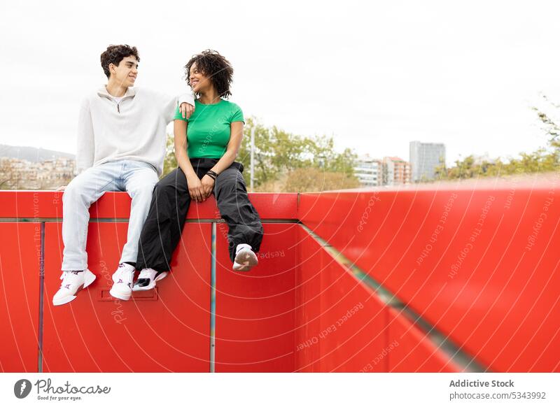 Glückliches buntes Paar auf rotem Zaun sitzend Mann ruhen selbstbewusst Sonnenlicht Windstille wolkenlos Sommer Stil Partnerschaft sich[Akk] entspannen