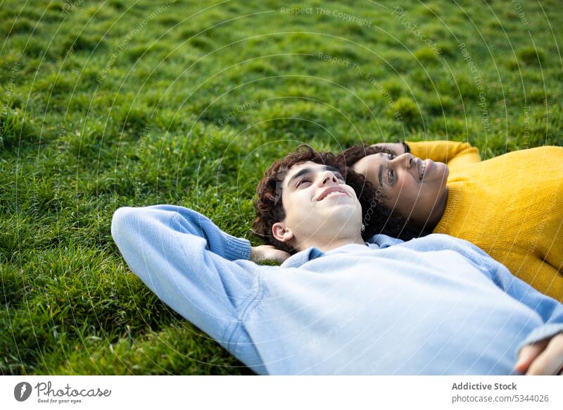 Glückliche diverse Freunde liegen auf Gras im Park Mann Frau Lügen Freundschaft Lächeln Hand hinter dem Rücken sich[Akk] entspannen Tageslicht tagsüber