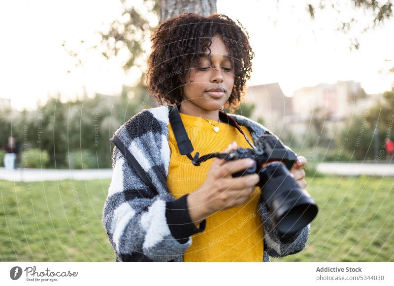 Schwarze Frau steht mit Fotokamera im Park Fotoapparat Fotograf professionell fotografieren Rasen Fotografie Fokus Konzentration Stadtbild Straße Gerät
