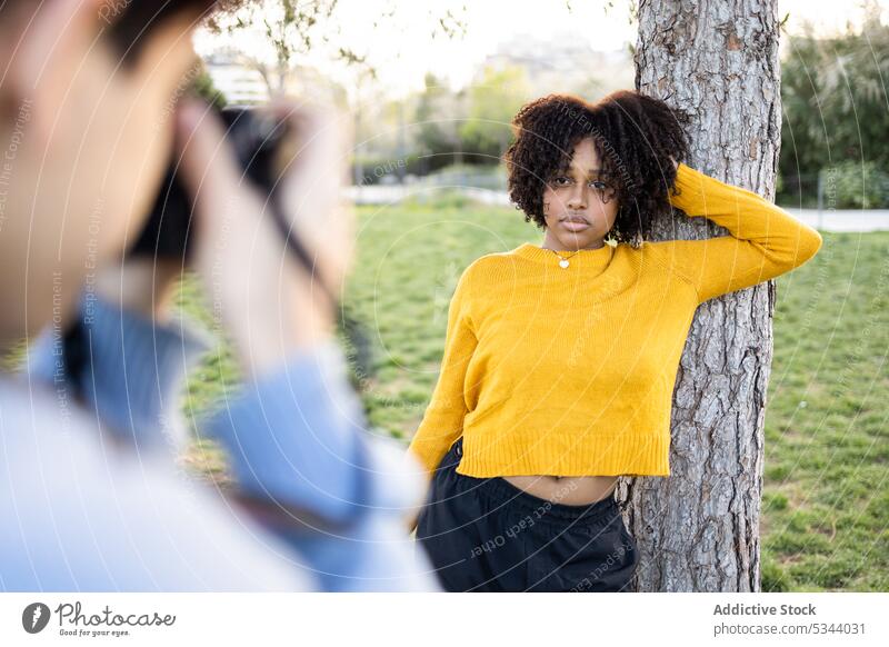 Schwarze Frau steht in der Nähe eines Baumes für ein Fotoshooting Mann Fotoapparat Fotograf fotografieren schießen Fotografie Moment Park Natur Gedächtnis