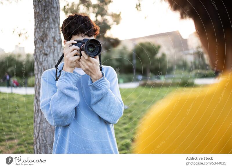 Junger Mann schießt Fotos in der Nähe eines Baumes auf grünem Gras fotografieren Fotoapparat Fotograf Park Fotografie Hobby Fotokamera schießen professionell