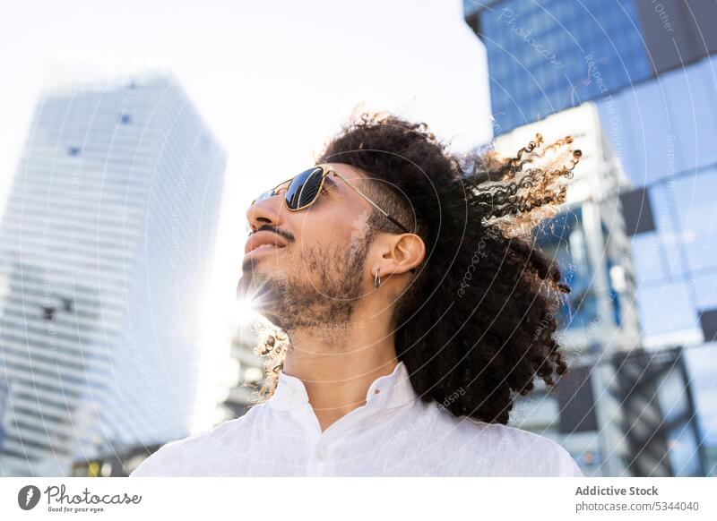 Lächelnder ethnischer Mann mit Brille, der in den Himmel schaut jung Browsen trendy Straße Großstadt maskulin Sonnenbrille benutzend Gerät männlich schwarz