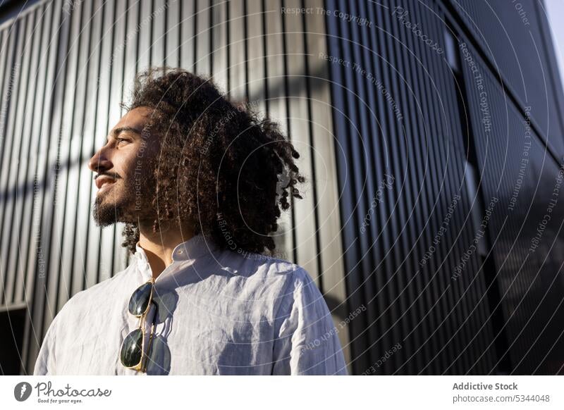 Glücklicher ethnischer Mann mit lockigem Haar schaut weg Straße selbstbewusst Großstadt besinnlich Afro-Look Apparatur krause Haare männlich Afroamerikaner