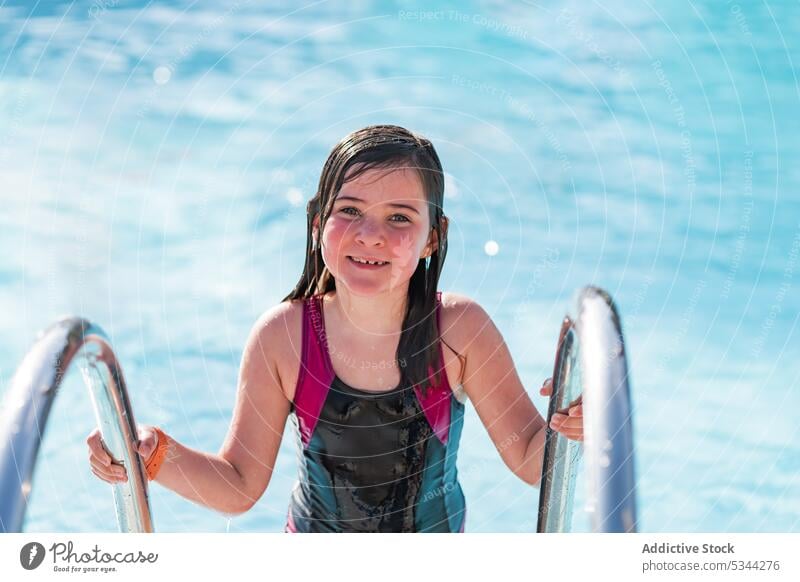 Lächelndes Mädchen schaut in die Kamera im Schwimmbad Pool Sommer Resort Urlaub Feiertag Badebekleidung Glück schwimmen Wasser Badeanzug Kind Sonne Beckenrand