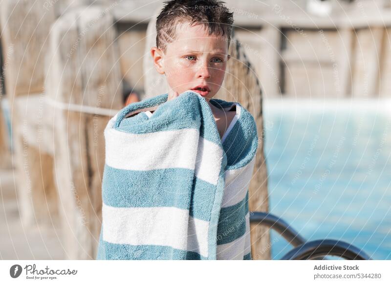 Niedlicher Junge im Handtuch am Pool Resort Sommer Beckenrand Urlaub Feiertag Kind Zaun tropisch Windstille ruhen Erholung Sonne Wochenende umhüllen hölzern