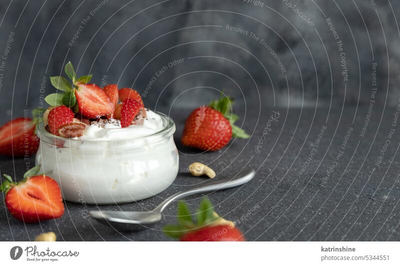 Glasgefäß mit griechischem Joghurt, Nüssen und Erdbeeren auf grauem Tisch mit einem Löffel, Nahaufnahme, Kopierraum Muttern erdbeeren Frühstück abschließen
