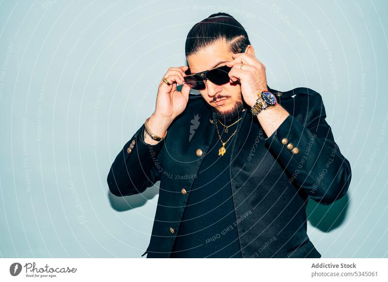 Selbstbewusster Mann, der eine Sonnenbrille vor blauem Hintergrund berührt Mode Stil cool Model Porträt Jacke trendy Vorschein Accessoire männlich Haarschnitt