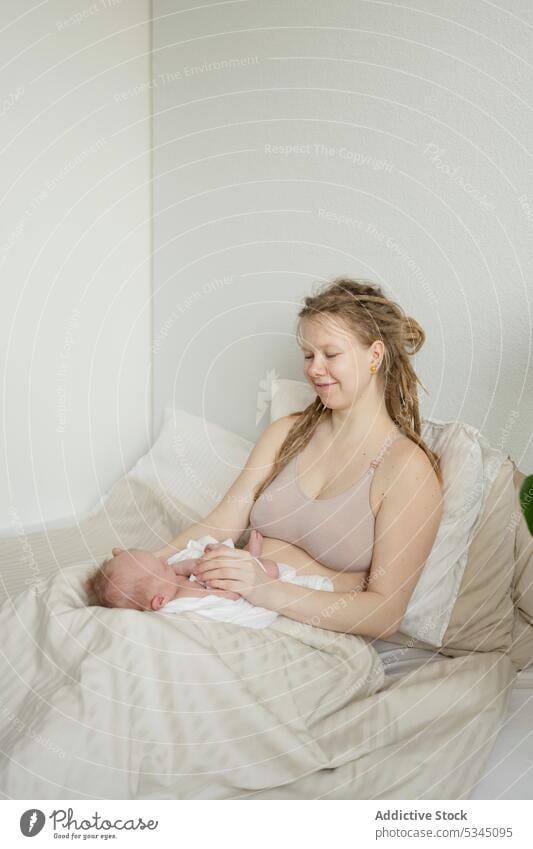Mutter sitzt mit Baby auf dem Bett Frau Säugling neugeboren Mama Kinderbetreuung mütterlich gemütlich Komfort unschuldig Mutterschaft Zusammensein Bettwäsche
