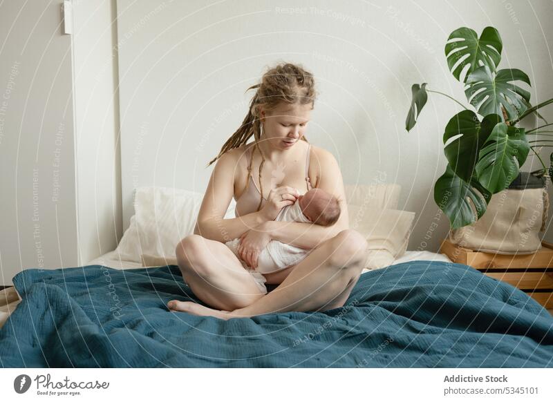 Frau stillt Säugling auf dem Bett sitzend Mutter Baby stillen neugeboren Mama Kinderbetreuung gemütlich Komfort unschuldig Mutterschaft Zusammensein Bettwäsche