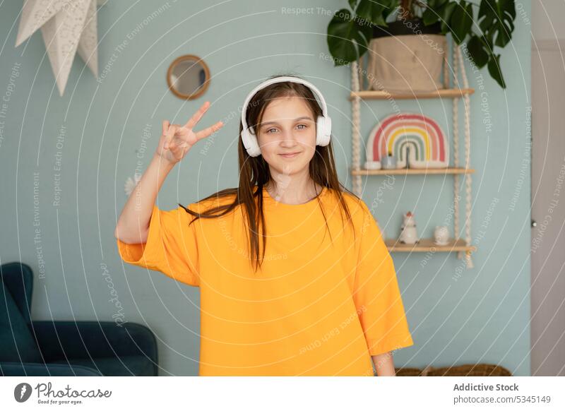 Fröhliches Kind mit Friedenszeichen Mädchen Musik zuhören v-Zeichen Tanzen gestikulieren Kopfhörer Schlafzimmer Drahtlos benutzend positiv Frau Gerät heimwärts