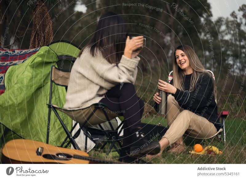 Freundinnen sitzen in Campingstühlen im Wald Frauen Lager Campingplatz Picknick reden Zelt Lächeln Wochenende jung heiter Sommer Freundschaft Wälder froh
