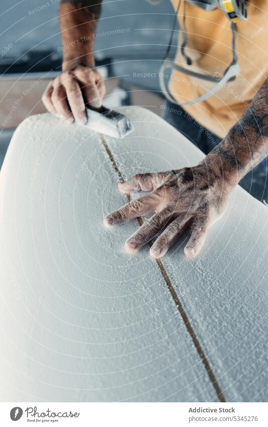 Ein Mann schleift ein Surfbrett mit professioneller Ausrüstung polnisch Werkzeug Meister Werkstatt Arbeit Holzplatte Instrument Grinden männlich Prozess Job